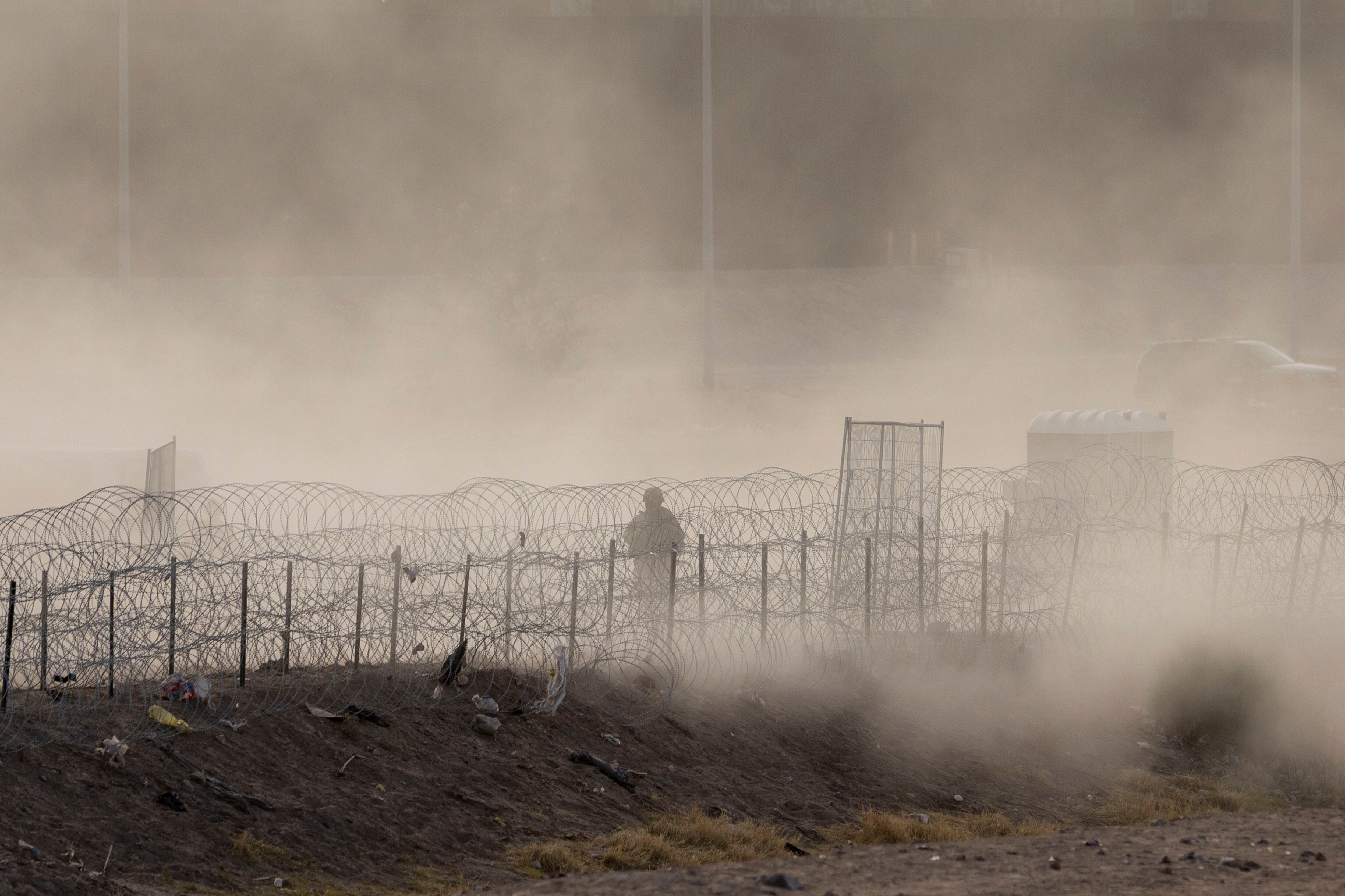 Three migrants who had managed to evade National Guard and cross the Rio  Grande onto U.S. territory wait for Border Patrol along a wall set back  from the geographical border, in El