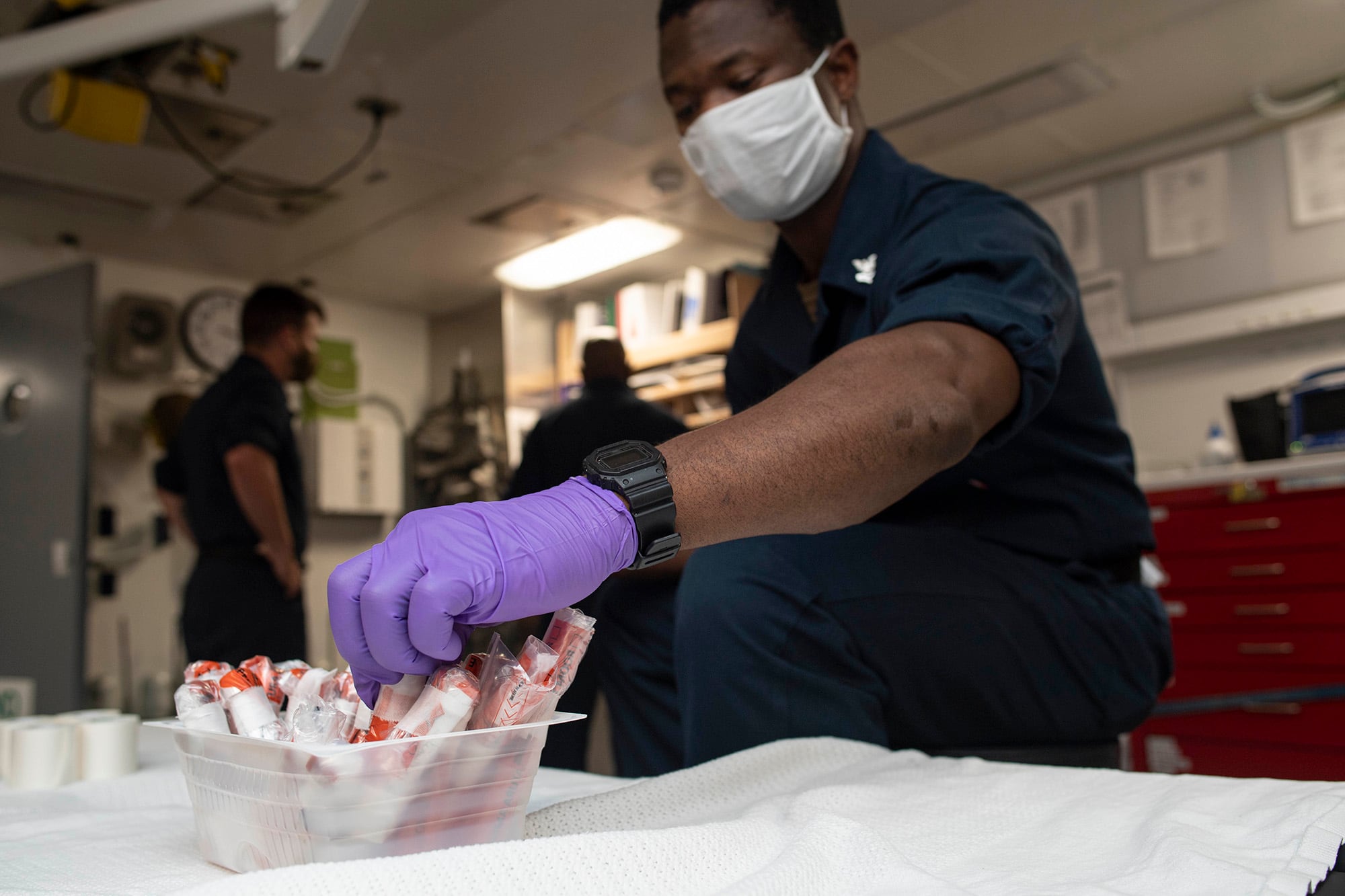 Hospital Corpsman 2nd Class Eric Hayford collects sealed COVID-19 test samples aboard the amphibious transport dock ship USS New Orleans (LPD 18) on Aug. 12, 2020, in the Sea of Japan.