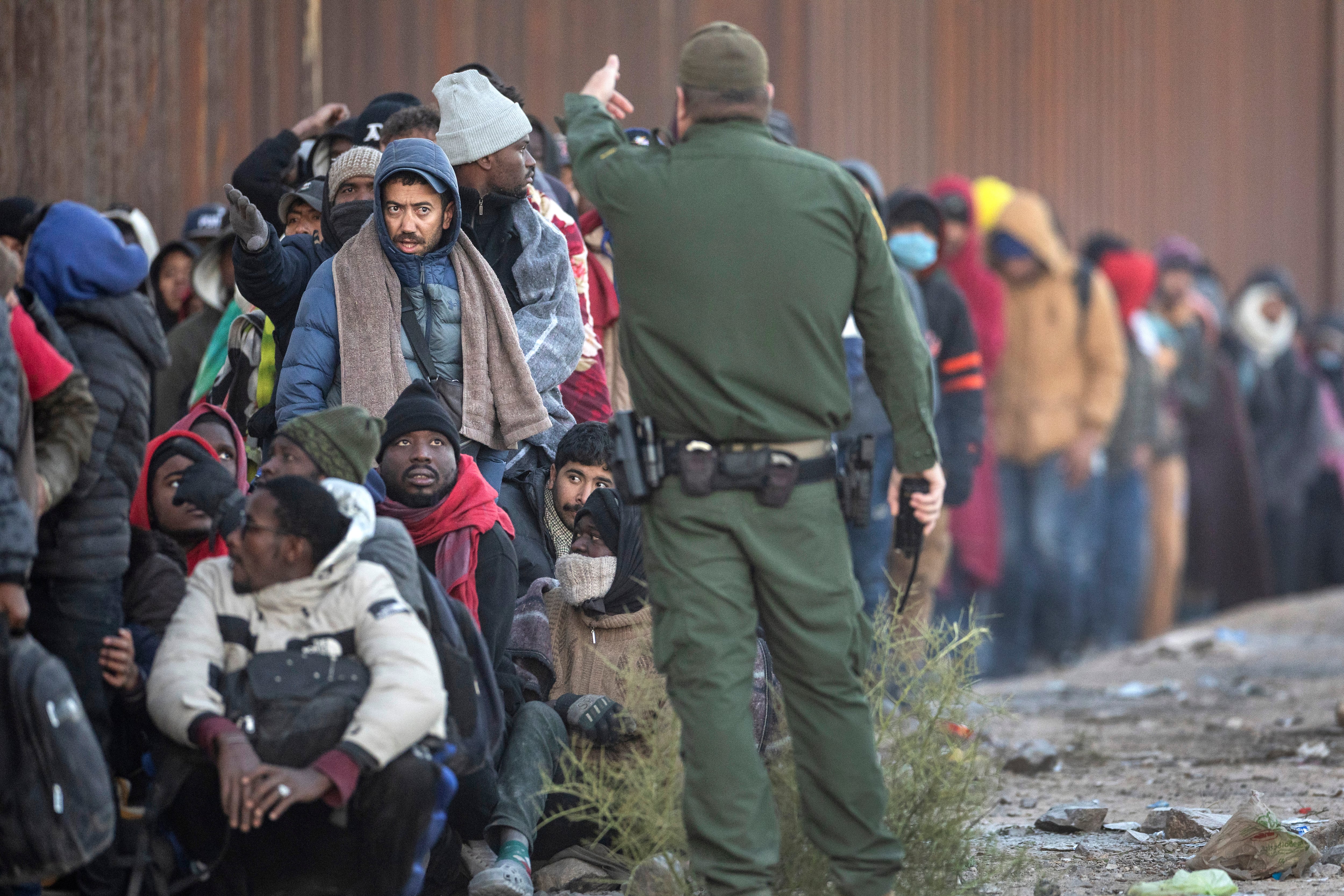 A U.S. Border Patrol agent asks immigrants to sit in a queue while they await transport from the U.S.-Mexico border on Dec. 6, 2023 in Lukeville, Arizona.