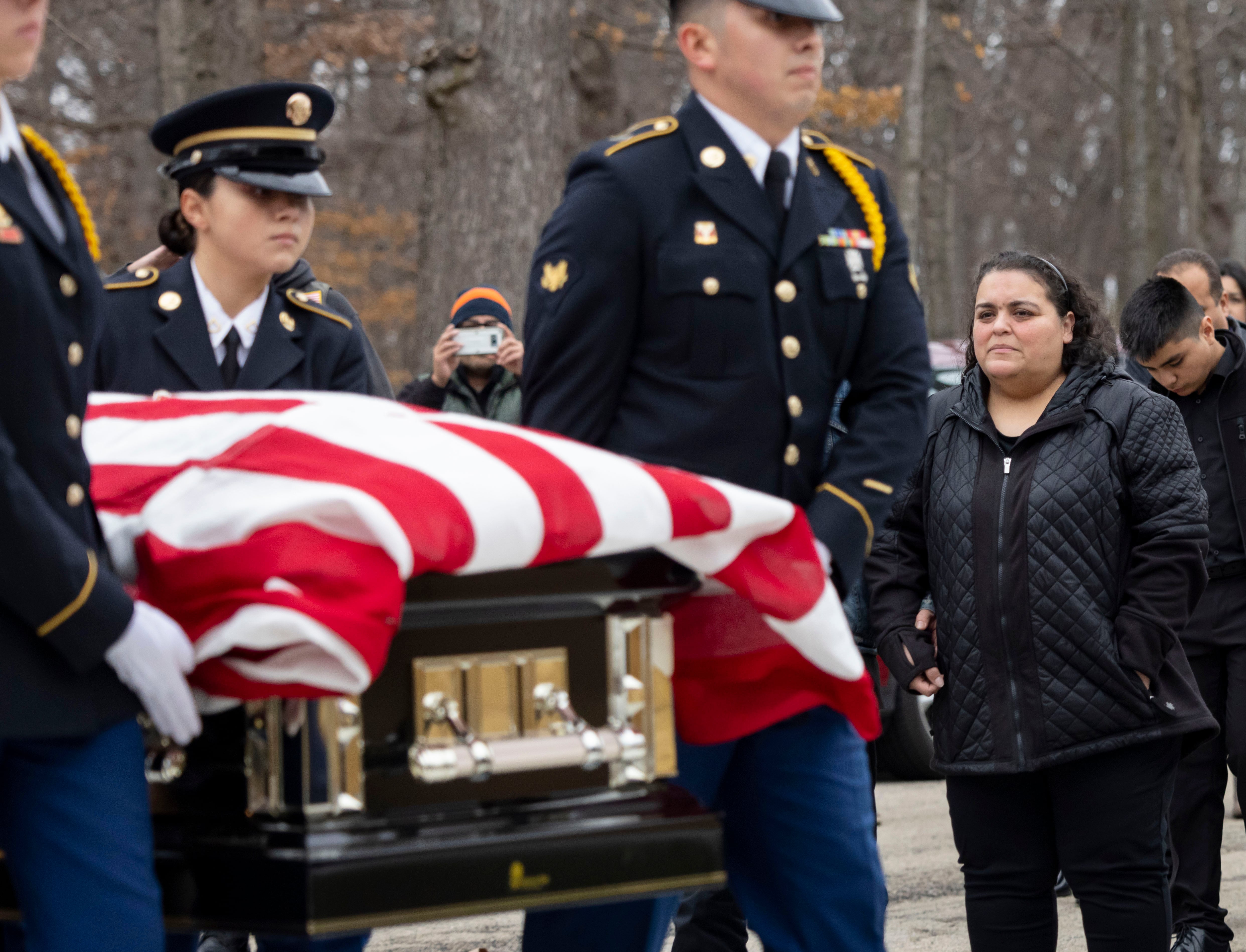 An honor guard carries the casket of former Army Sgt. Joel Gomez while sister Noemi Sanchez watches during funeral services at Abraham Lincoln National Cemetery on Tuesday, Nov. 29, 2022, in Elwood, Ill.