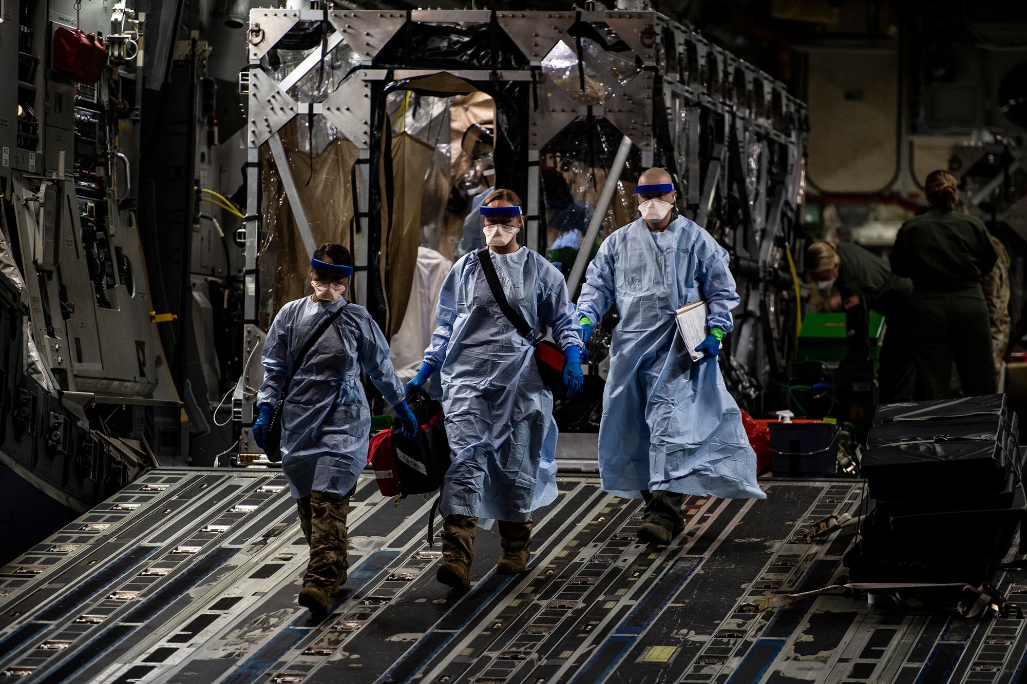 Three U.S. Air Force medical airmen exit a C-17 Globemaster III aircraft following the first-ever operational use of the Transport Isolation System at Ramstein Air Base, Germany, April 10, 2020.