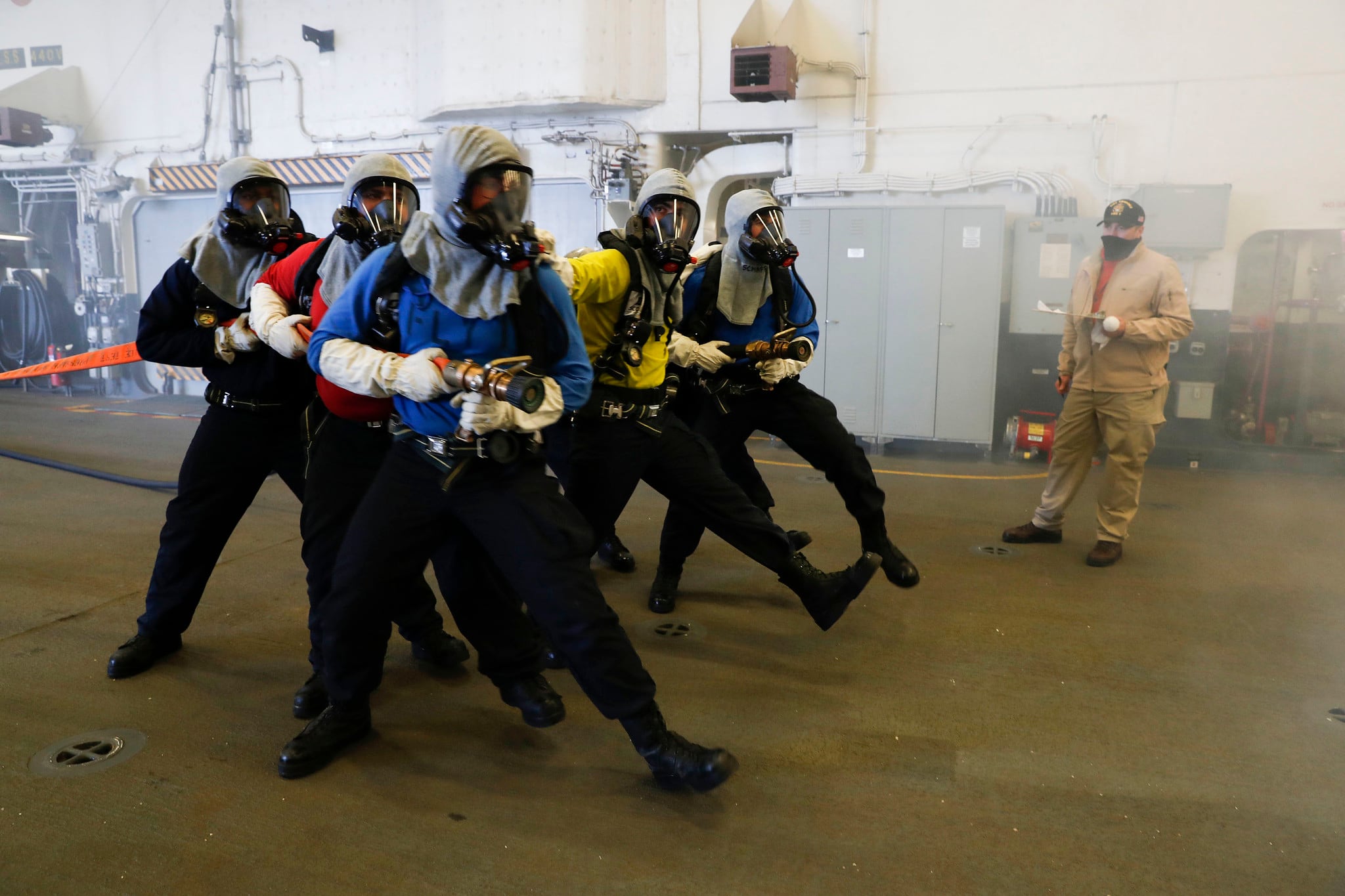 Aviation boatswain’s mates (handling) simulate approaching a fire during an aircraft firefighting drill in the hangar bay of the amphibious assault ship USS Tripoli (LHA 7), Aug. 31, 2020, in the Pacific Ocean.