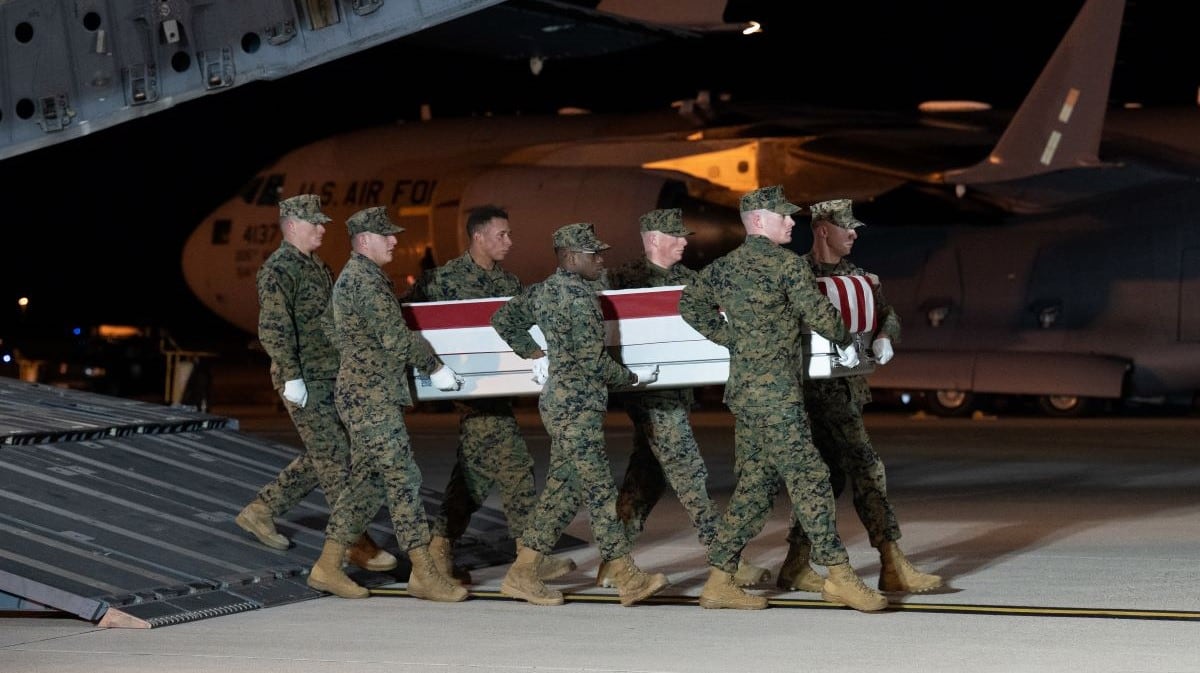 A team of Marines carrying a coffin off of an airplane at night