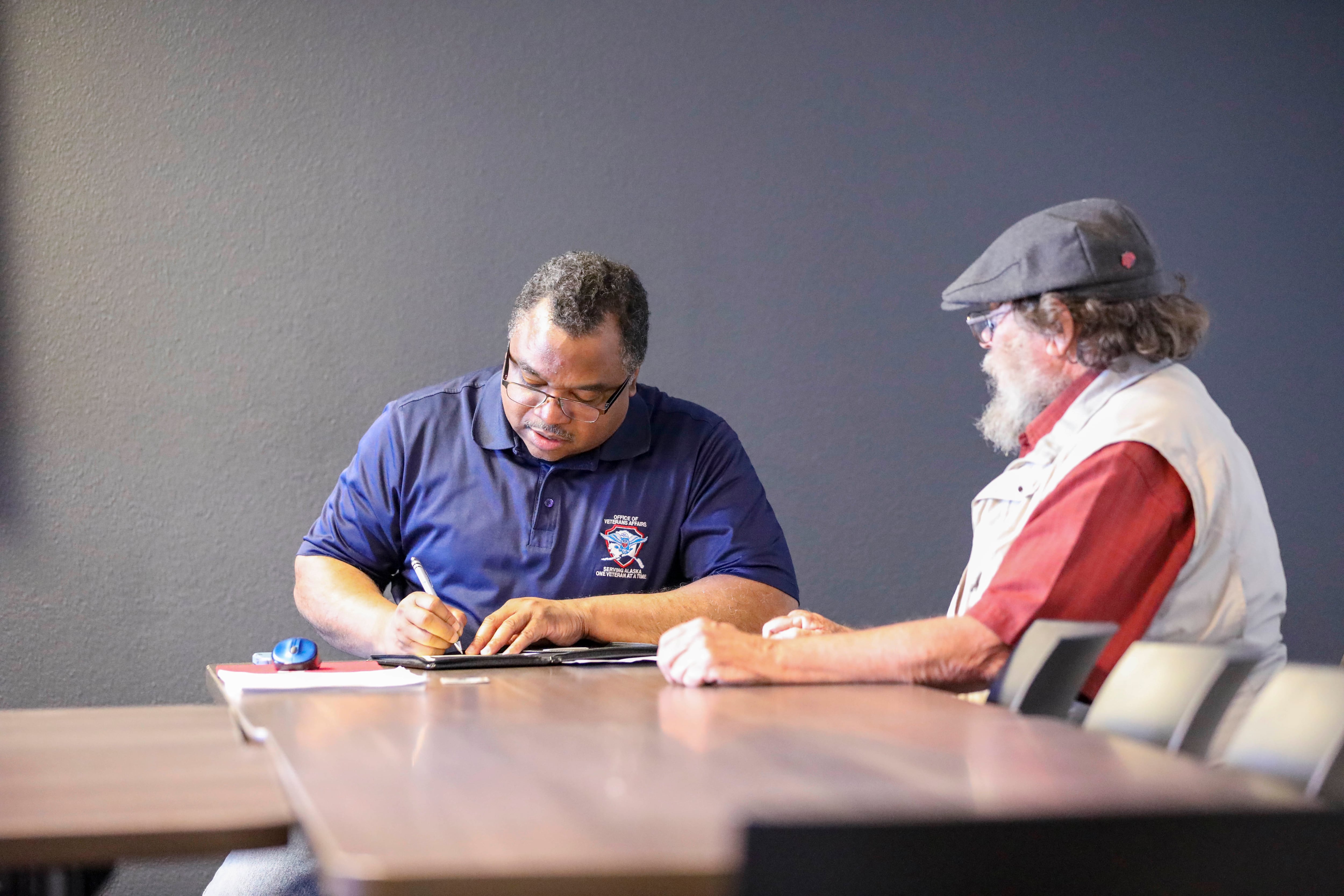 Forrest Powell, left, deputy director, state of Alaska Office of Veterans Affairs, assists local veterans with their earned benefits during an outreach event at the Aurora Inn in Nome, Alaska, July 9, 2022.