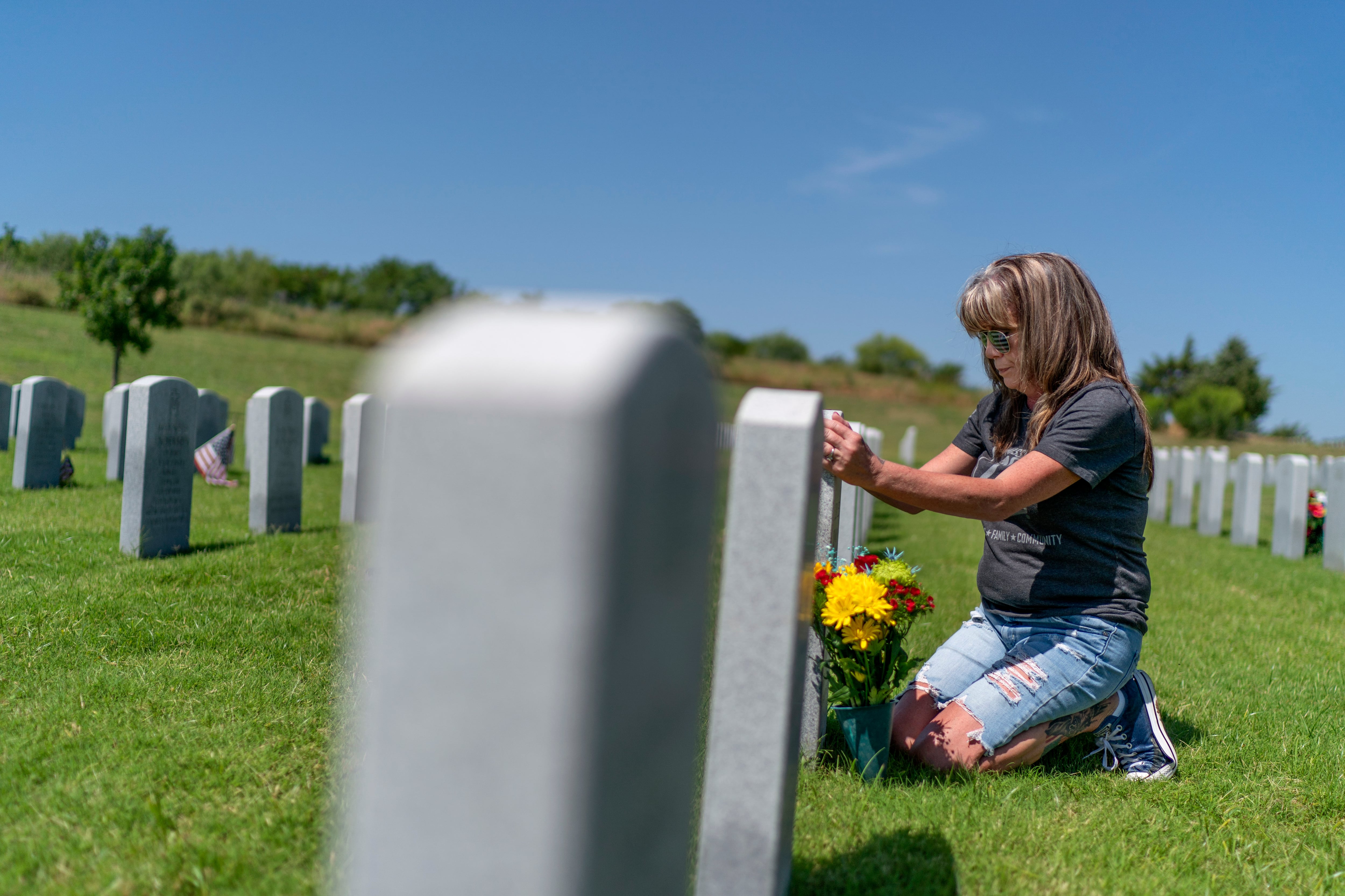 Barbie Rohde touches the tombstone of her son, Army Sgt. Cody Bowman, at the Dallas-Fort Worth National Cemetery, Sunday, June 11, 2023, in Dallas.