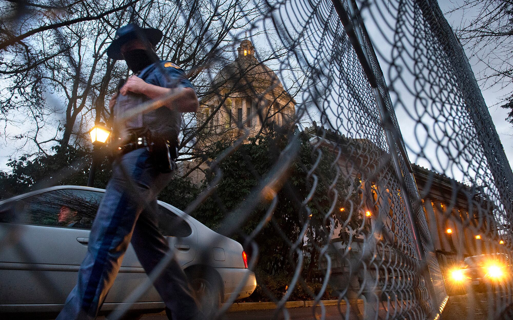 A Washington State Patrol trooper walks past new security fencing installed on Friday, Jan. 8, 2021, around the state Capitol in Olympia, Wash., in anticipation of the legislative session opening on Monday.